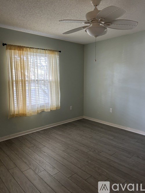 A room with a ceiling fan and a window with curtains.
