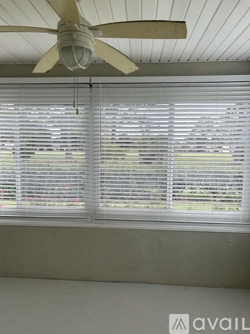 A ceiling fan hangs over a window with white blinds.