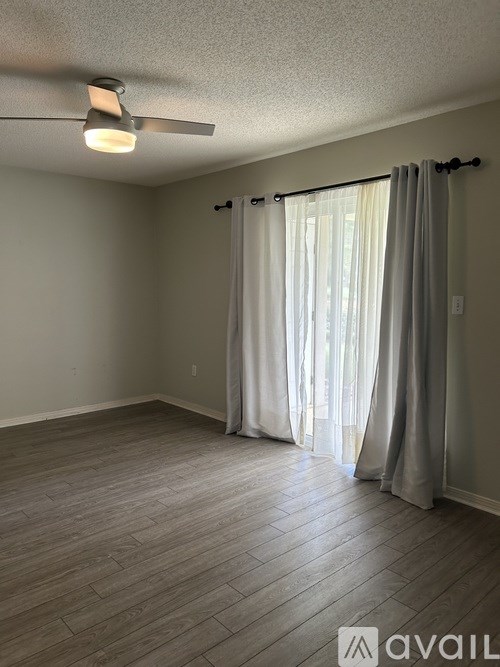 A room with a ceiling fan and a window with curtains.
