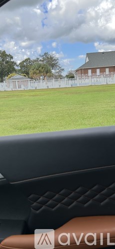 A car's interior with a brown leather seat and a window showing a grassy field and a building.