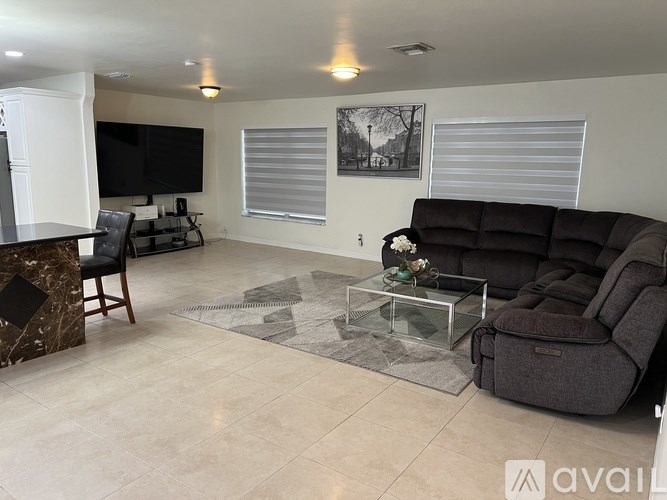 A living room with a black sofa, a glass coffee table, and a television.