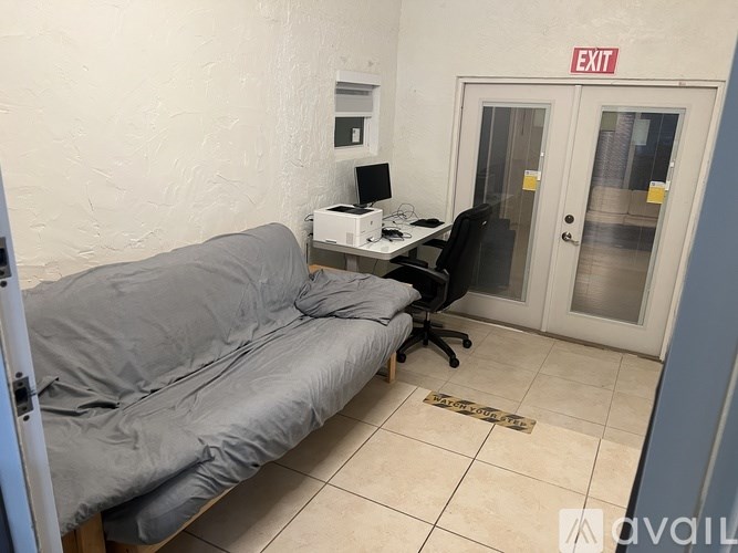 A grey couch is in a room with a white wall and a red exit sign.