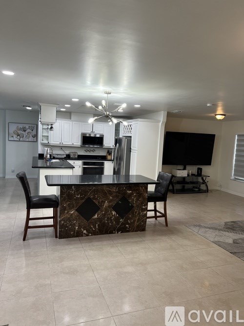 A modern kitchen with a marble island and black chairs.