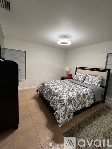 A bedroom with a bed, nightstand, and a window with blinds.