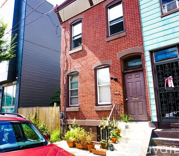 A red car is parked in front of a red brick house.