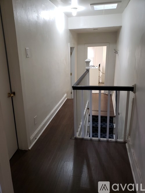 A hallway with a black railing and wooden floors.