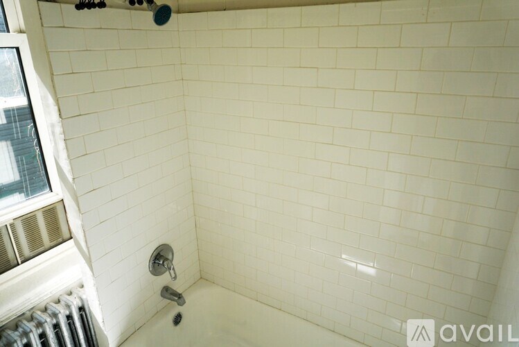 A white tiled shower area with a silver faucet.