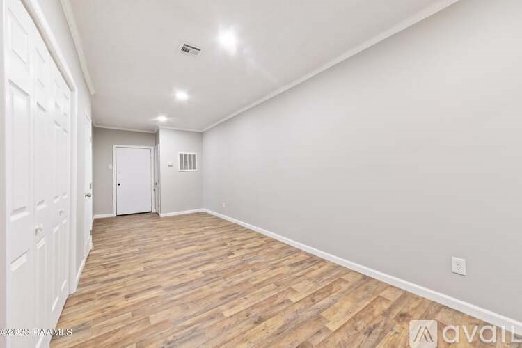 A room with wooden flooring and white walls, with a door at the end of the room.