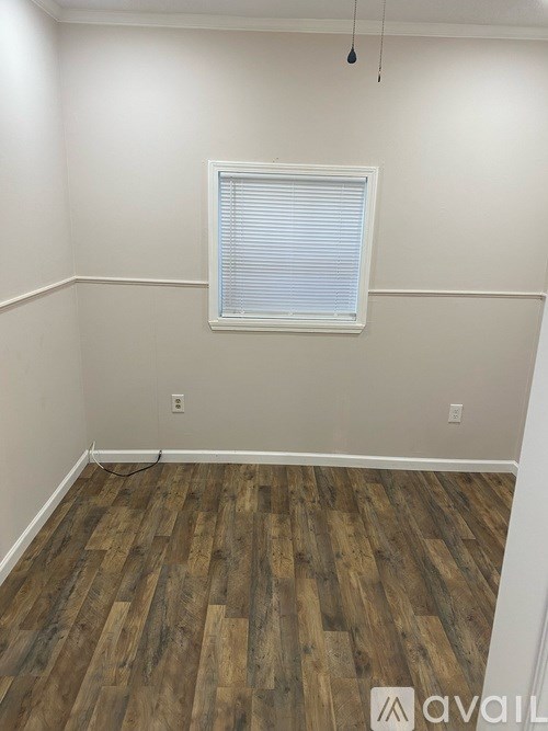 A room with wooden flooring and a window with blinds.