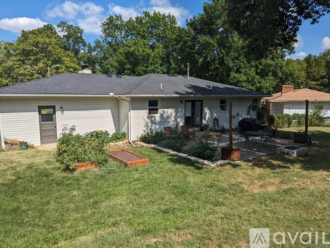 A house with a grey roof and a white exterior is surrounded by a green lawn and trees.