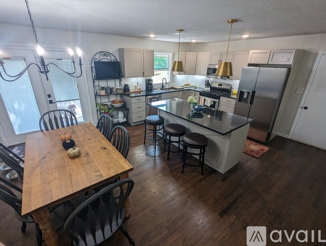 A kitchen with a wooden table and chairs in the foreground and a refrigerator, microwave, and other appliances in the background.