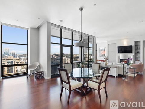 A modern living room with a glass table and chairs, a television, and a view of the city.