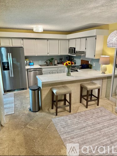A kitchen with a refrigerator, bar stools, and a counter.