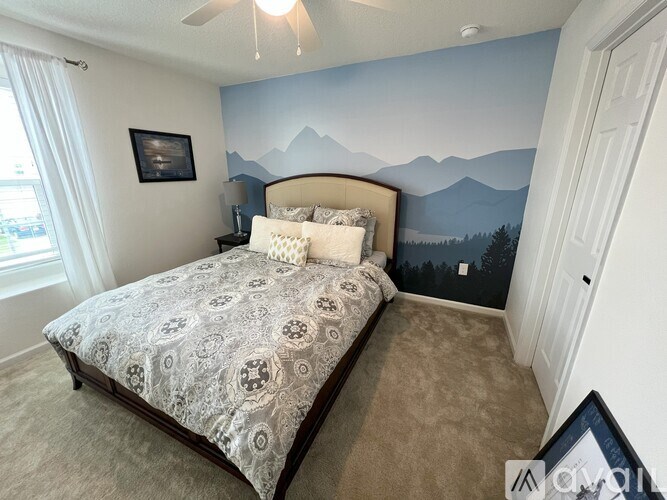 A bedroom with a bed, a ceiling fan, and a mountain mural on the wall.