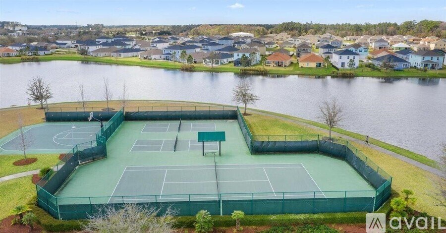 A tennis court surrounded by a fence with houses in the background.