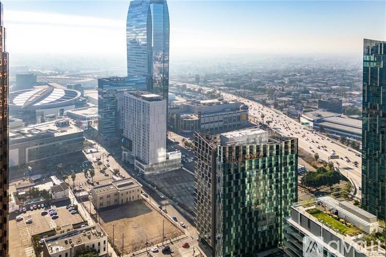 A cityscape with a mix of modern and older buildings, a clear sky, and a busy road with vehicles.