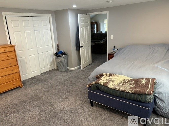 A bedroom with a bed, dresser, and a trash can.