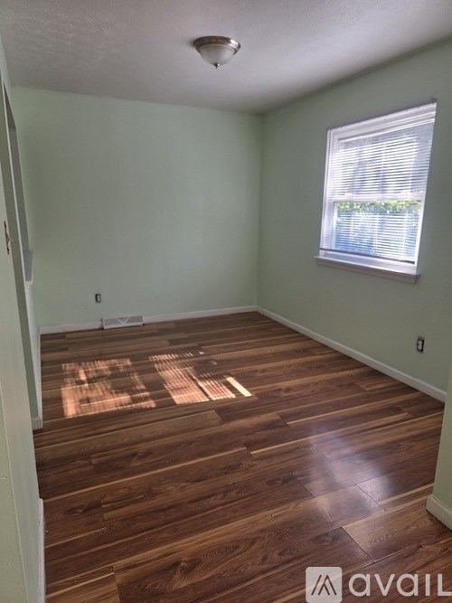 A room with wooden flooring and a window with blinds.