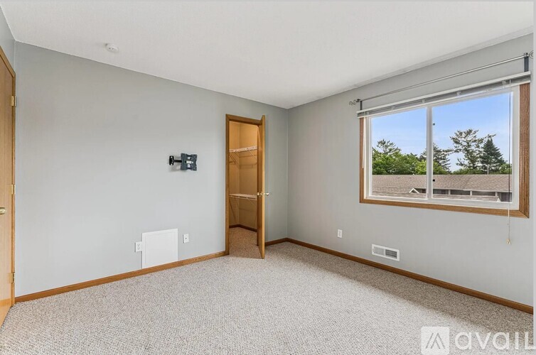 A room with a carpeted floor, a window with a view of trees, and a door leading to another room.