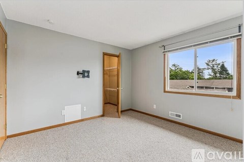 A room with a carpeted floor, a window with a view of trees, and a door leading to another room.