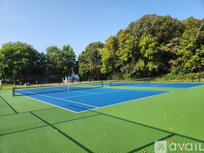 A tennis court surrounded by trees under a clear blue sky.