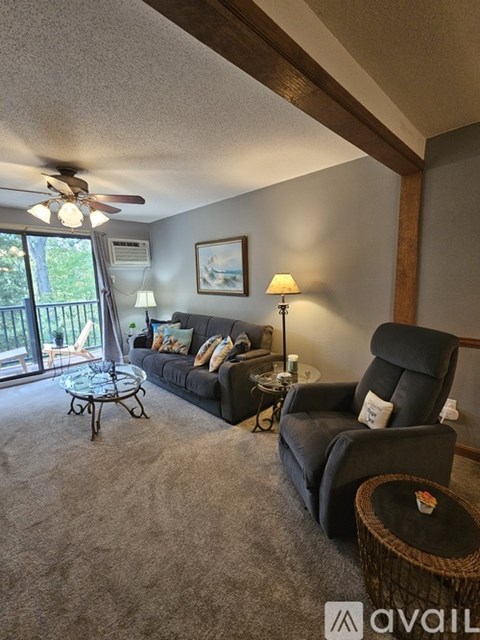A living room with a black couch, a black chair, a glass table, and a ceiling fan.