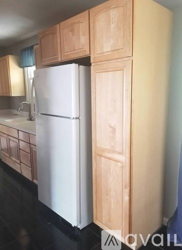 A white refrigerator stands next to a wooden cabinet in a kitchen.