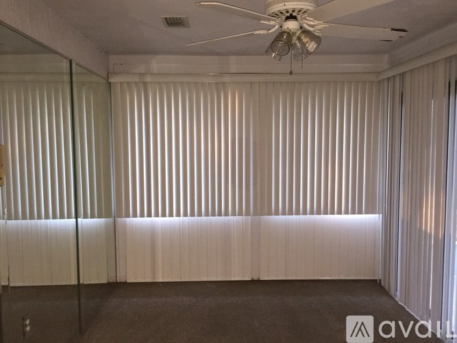 A room with a ceiling fan and light, a glass wall, and a carpeted floor.