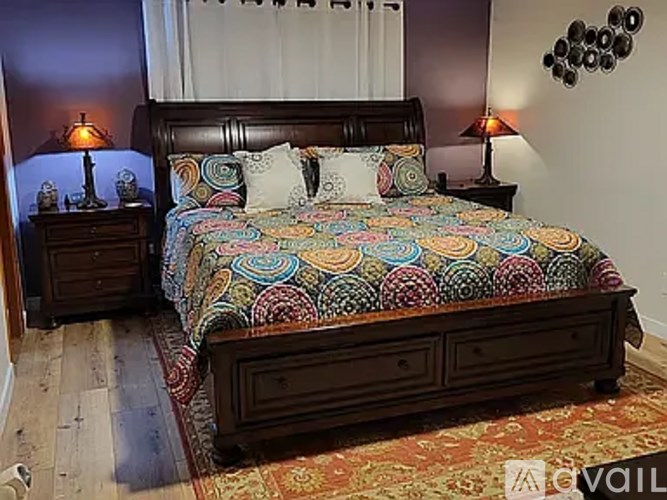 A bed with a colorful comforter and two nightstands with lamps.