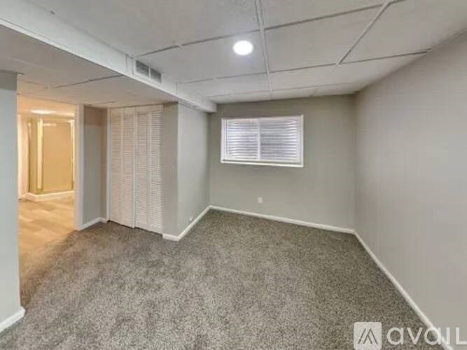 A room with a carpeted floor and a window with blinds.
