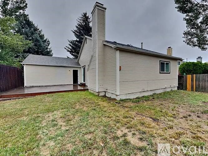 A house with a grey roof and a chimney is surrounded by a grassy area.