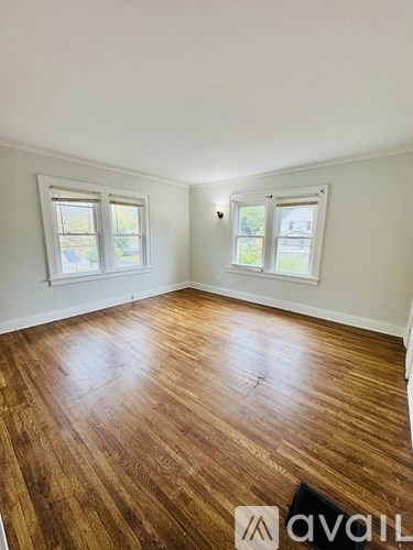A room with wooden flooring and two windows.