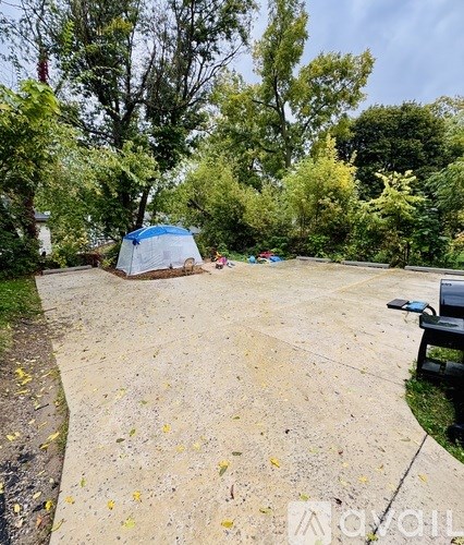A blue tent is set up in a park with a bench and trees in the background.