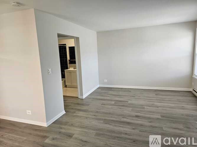 A room with wooden flooring and white walls, with a doorway leading to another room.