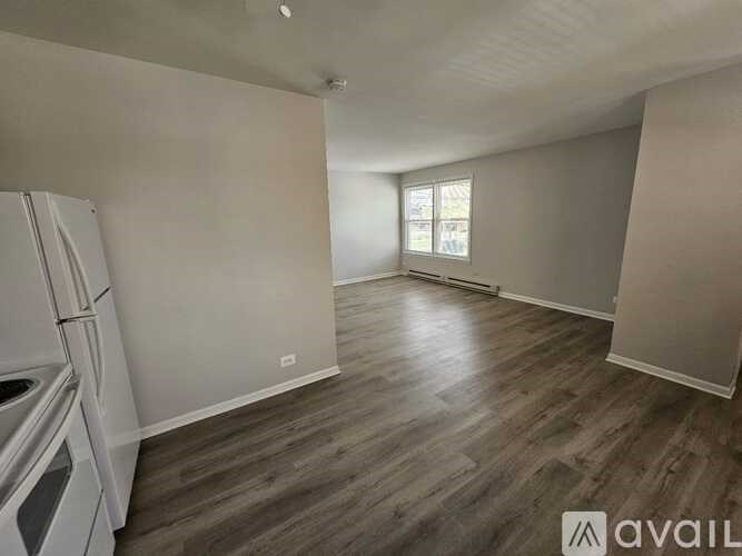 A kitchen with a refrigerator and a window in a room with wooden flooring.