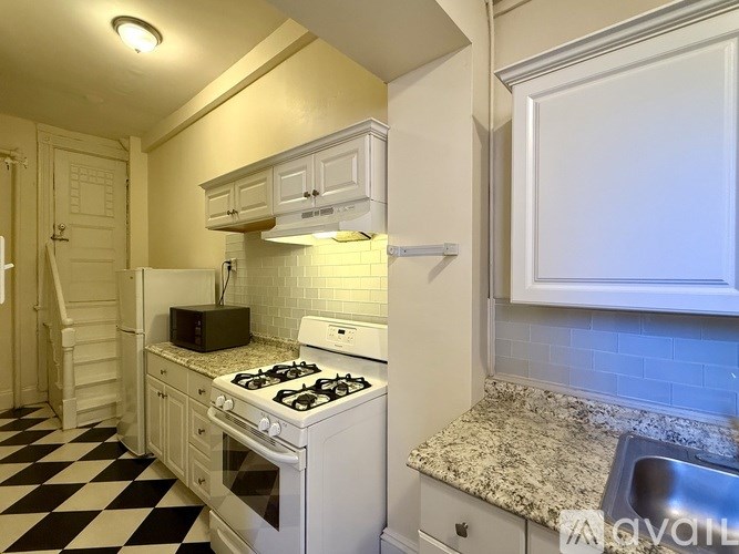 A hallway with a black and white checkered floor leads to a bathroom.