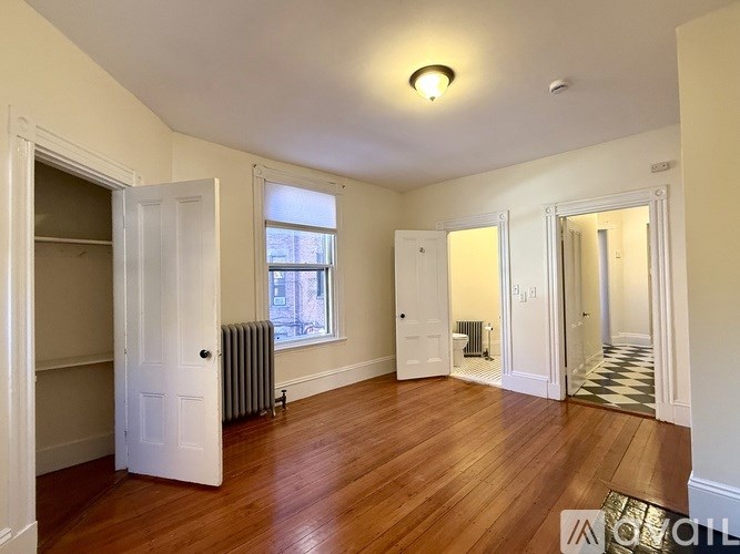 A room with wooden flooring and white walls, with a doorway leading to another room.