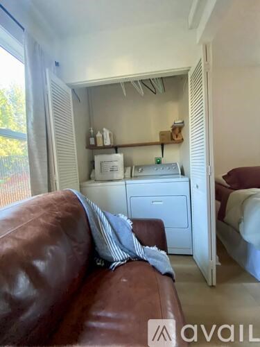 A brown leather couch sits in a room with a white cabinet and a bed in the background.