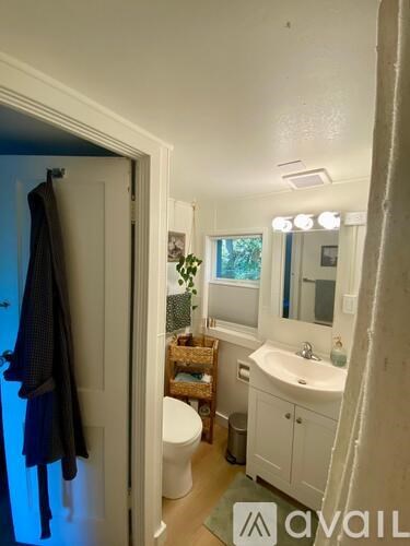 A bathroom with a toilet, sink, mirror, and a window.