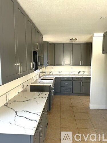 A kitchen with marble countertops and grey cabinets.