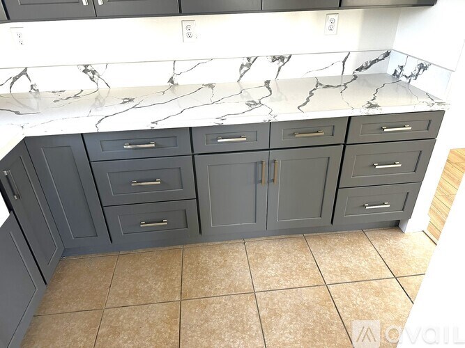 A kitchen with marble countertops and grey cabinets.