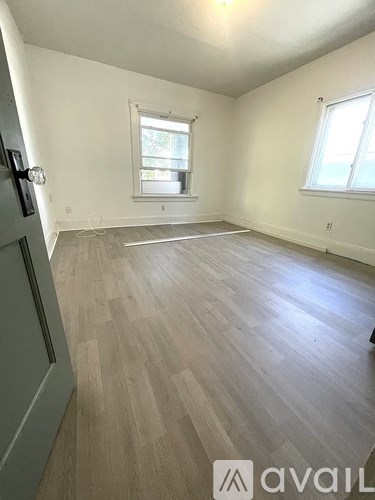 A room with wooden flooring and two windows.