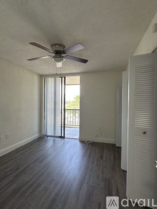A room with a ceiling fan and sliding glass doors leading to a balcony.