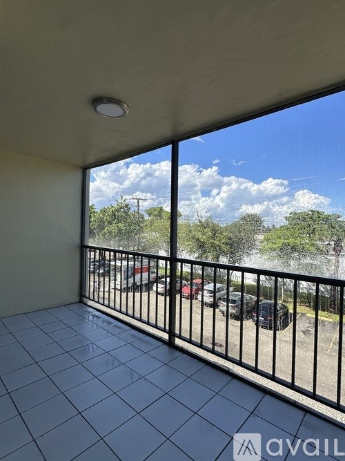 A balcony with a black railing and a view of a parking lot and trees.