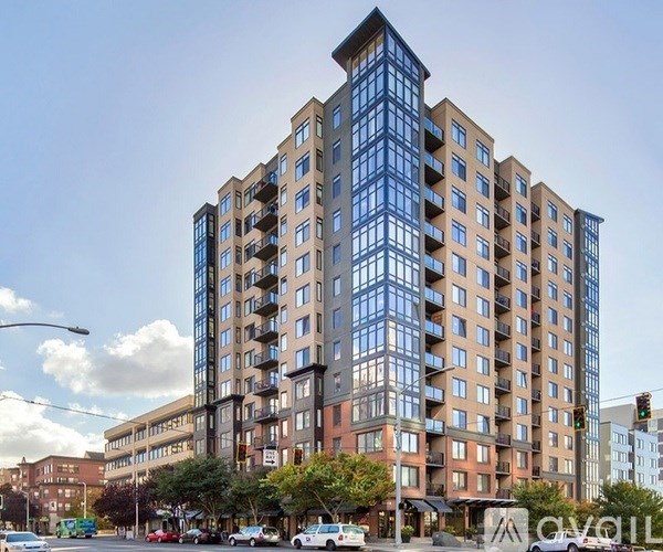 A tall apartment building with many windows and balconies is located on a street corner with cars parked along the curb.