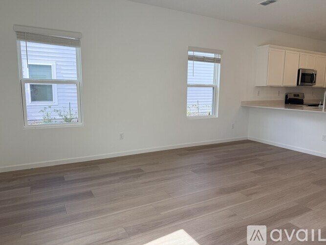 A room with wooden flooring and two windows.