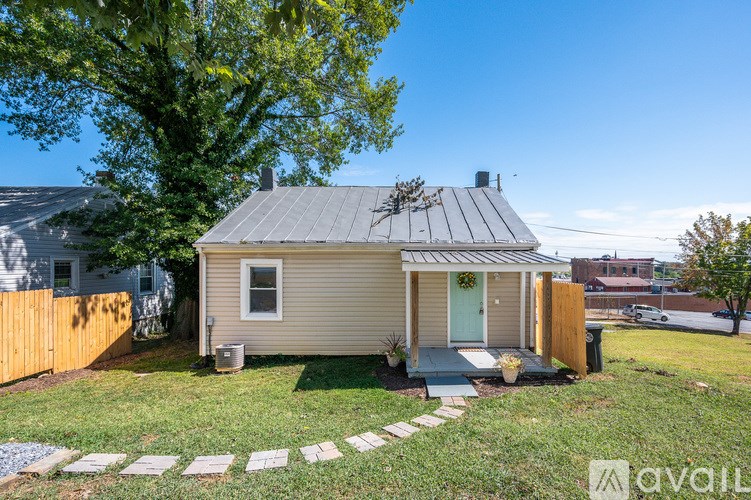 A small house with a grey roof and a green door is surrounded by a wooden fence and a small garden.