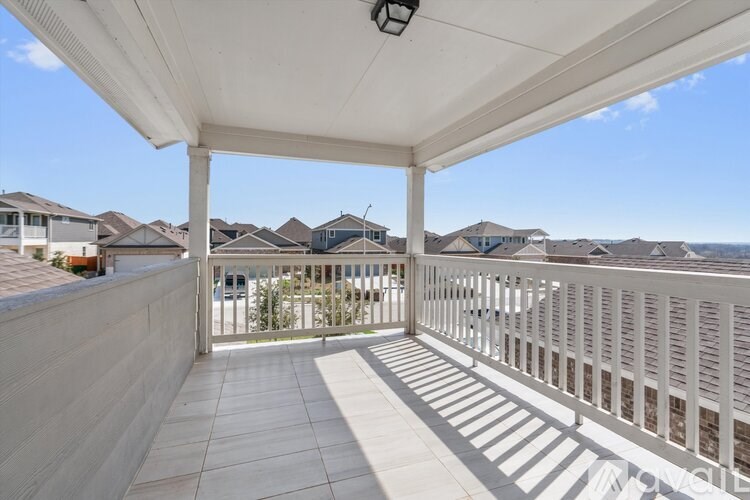 A white covered balcony with a railing and a view of houses in the distance.