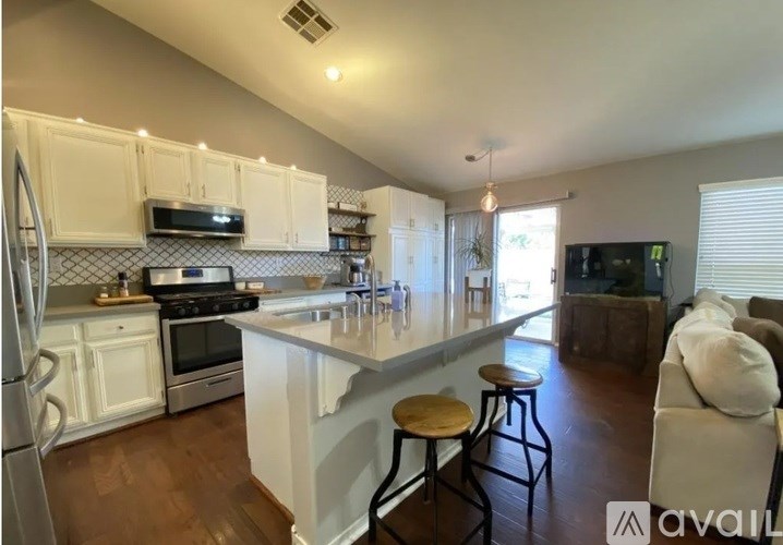 A kitchen with white cabinets and a white island with a countertop and bar stools.