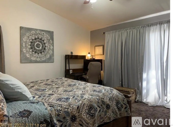 A bedroom with a patterned bedspread and a grey curtain.